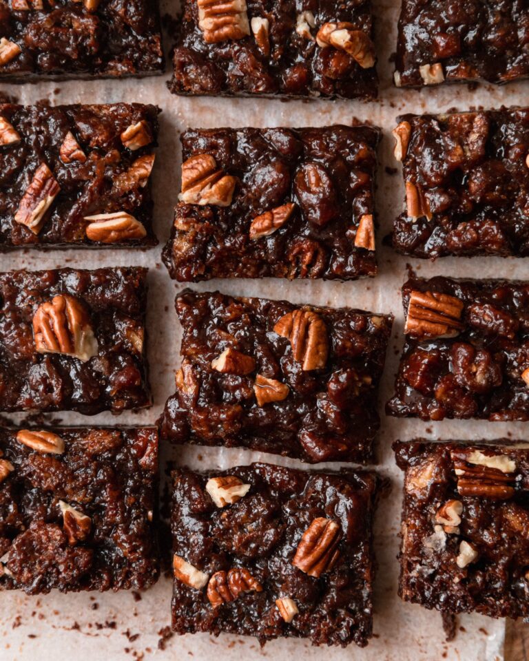 An overhead shot shows gooey chocolate pecan bars on top of parchment paper.